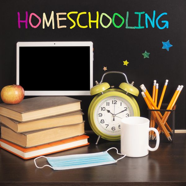 Homeschooling setup with books, tablet, clock, and school supplies.
