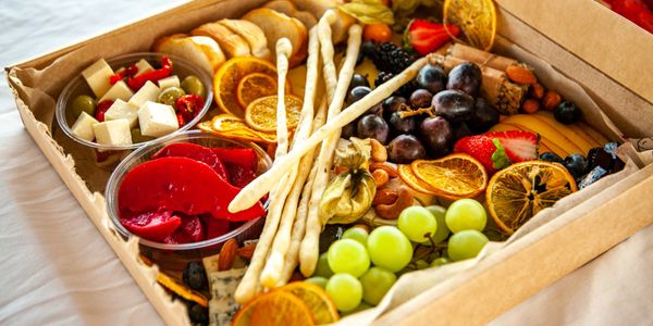 A vibrant charcuterie box with fruits, cheese, nuts, and breadsticks.
