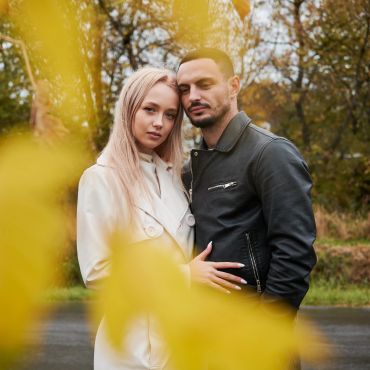 Couple posing outdoors with yellow leaves in foreground.