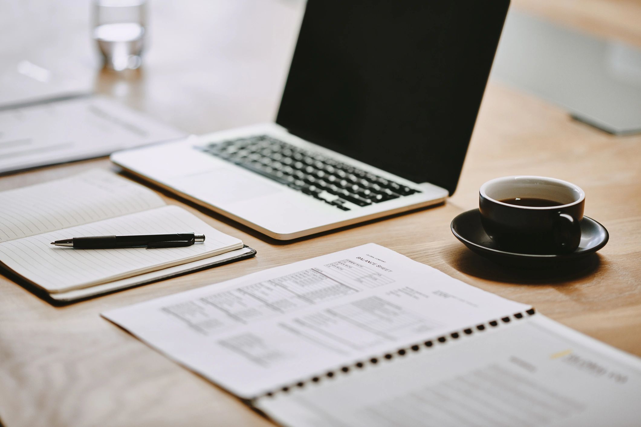 Workspace with laptop, notebook, pen, coffee, and documents on a wooden desk.