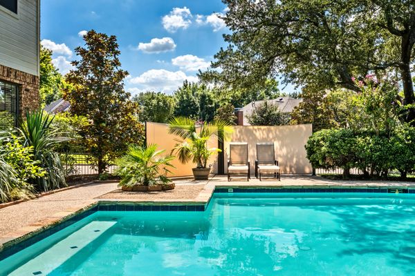 Sunny backyard pool area with two lounge chairs and lush greenery.