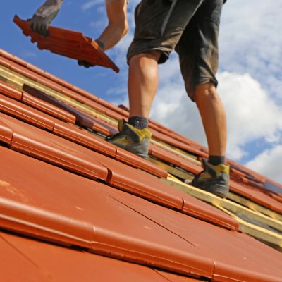 Worker installing red roof tiles on a sunny day.