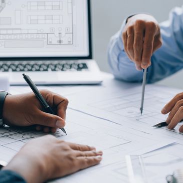 Two people working on architectural blueprints with a laptop displaying plans.