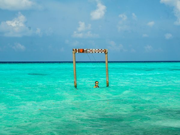 A person stands in turquoise water near a sign reading 'I love Thoddoo'.