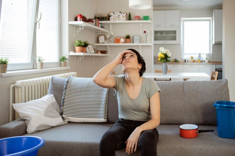 Young woman collecting leaking water from the ceiling at home