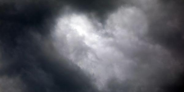 Heart-shaped break in dark storm clouds revealing light.