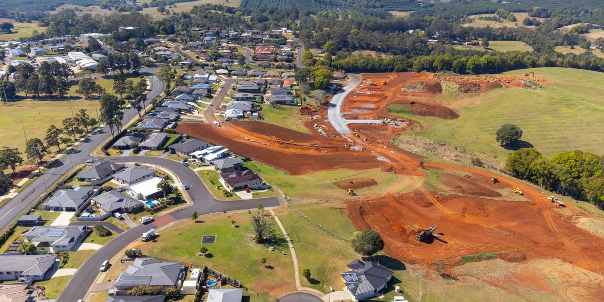 Aerial view of suburban homes next to a large construction site with red soil.