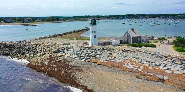 Coastal lighthouse with rocky shore and boats in background.