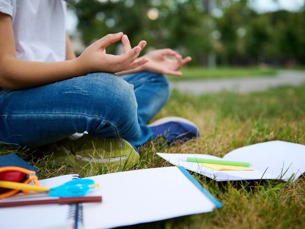 Person meditating outdoors surrounded by school supplies on grass.