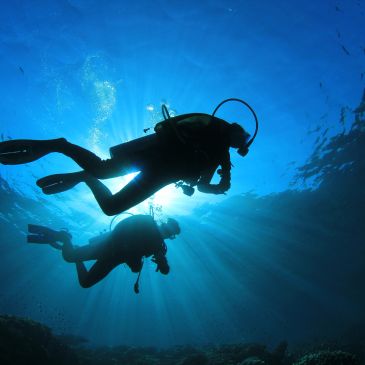 Silhouette of two scuba divers underwater with sun rays