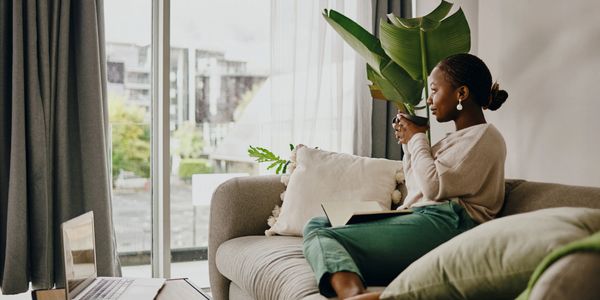 Woman relaxing on a couch with a cup in hand by the window.