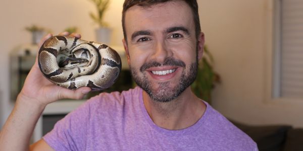 Man smiling while holding a coiled snake.