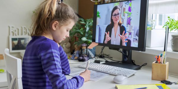 Young girl attending online class and writing notes.