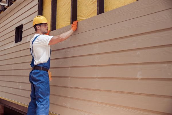 Construction worker installing wooden siding on a building.