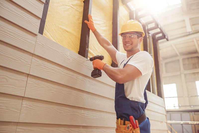Handsome young man construction worker looking at camera and smiling while installing exterior wood siding