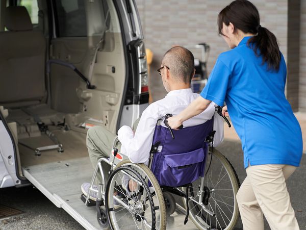 Caregiver assists elderly man in wheelchair onto accessible van.