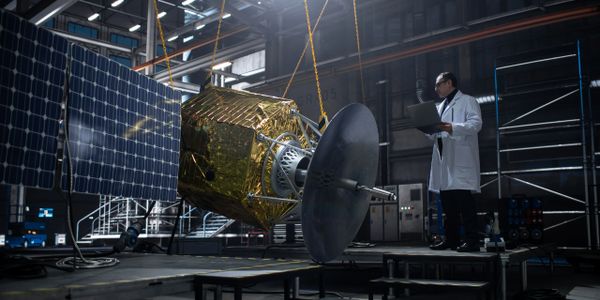 Engineer inspects a spacecraft with solar panels in a lab.