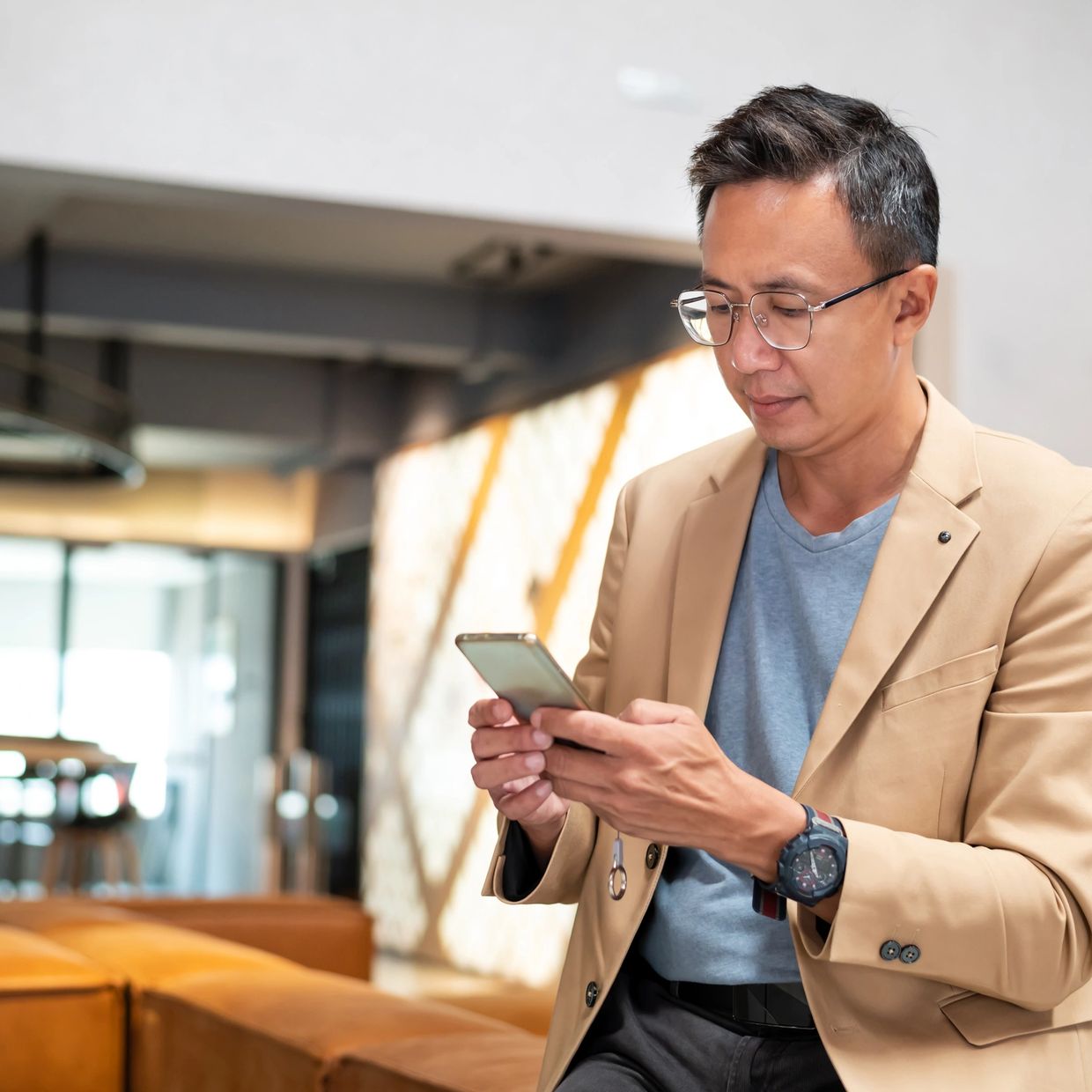 Man in a beige blazer using a smartphone indoors.