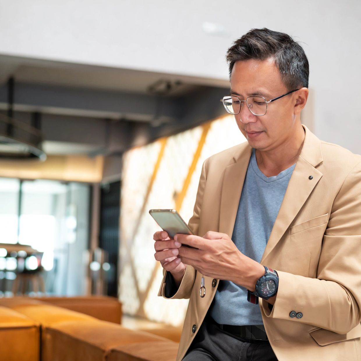 Man in a beige blazer using a smartphone indoors.