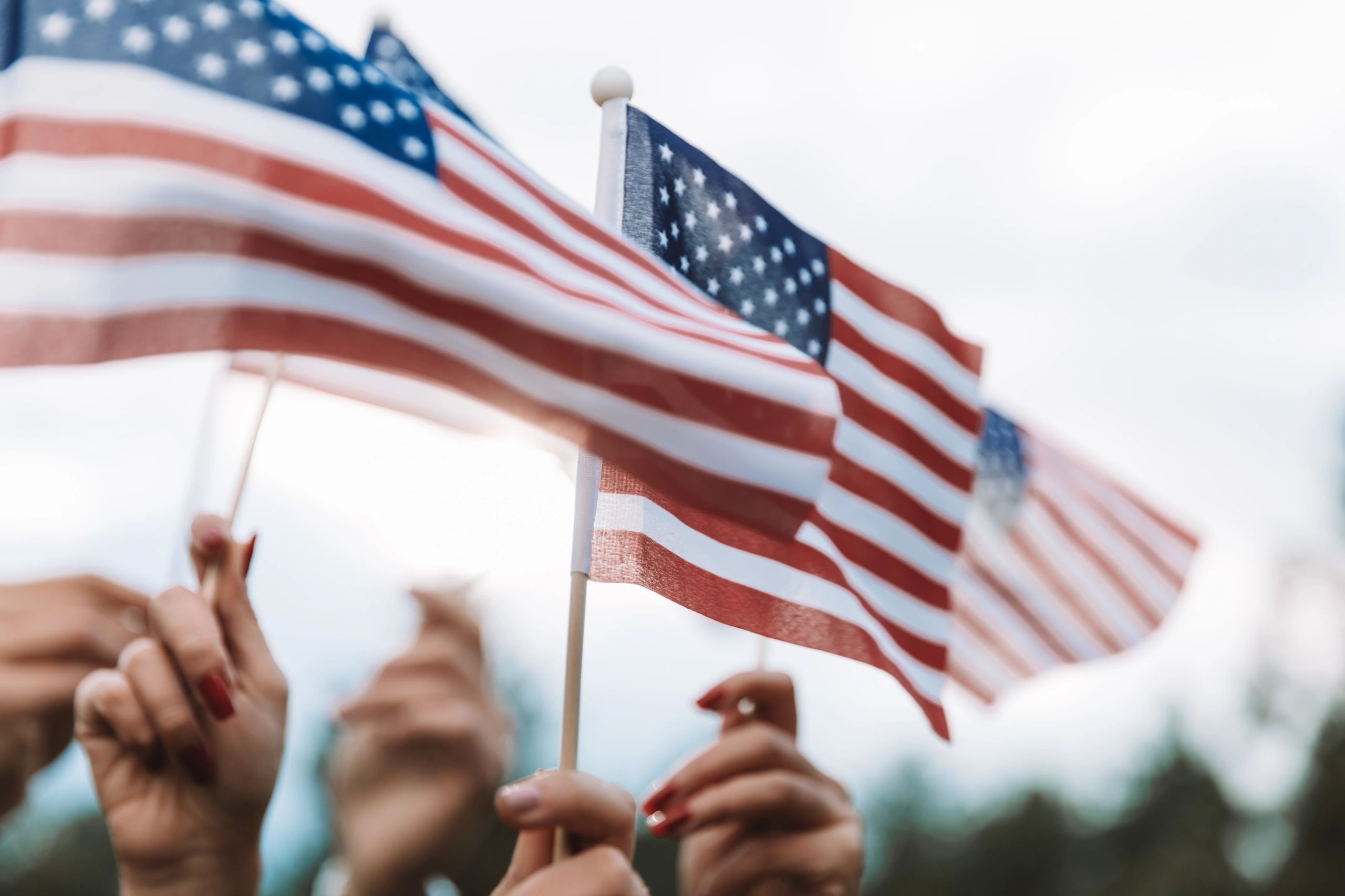 Hands waving small American flags outdoors.
