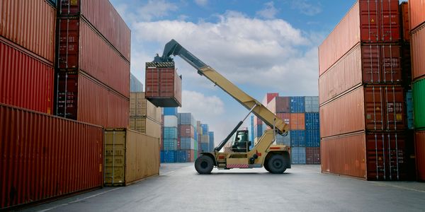 A forklift lifting a container in a shipping yard with stacked containers.