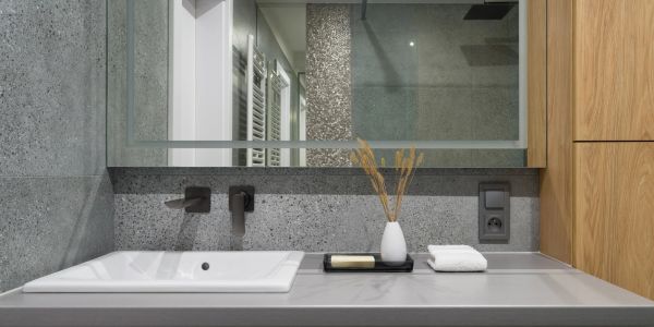 Modern bathroom sink with gray stone walls and wooden cabinet.