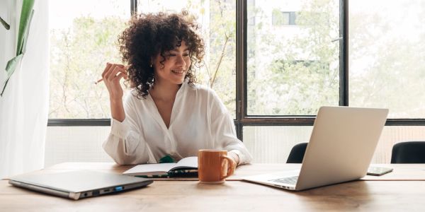 Young woman working on laptop at desk with coffee mug.