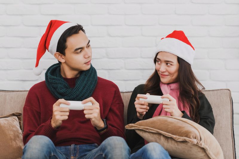 Young Asian couple lover wearing Santa Claus hat.playing video game together in room decorated with Christmas trees at home background.Christmas celebration concept.