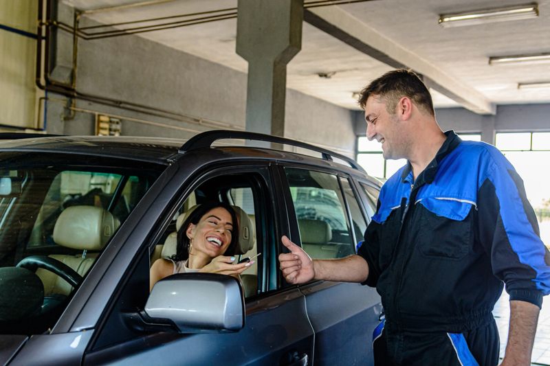 A Car Mechanic is Giving a Car Keys to a Businesswoman in Auto Workshop After Successful Repairing of the Car.