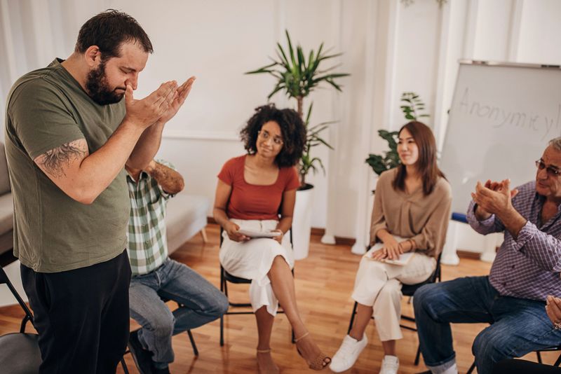 Diverse group of people, men and women with problems together, consoling a man on group therapy.