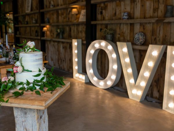 Wedding cake with lit LOVE sign in background.