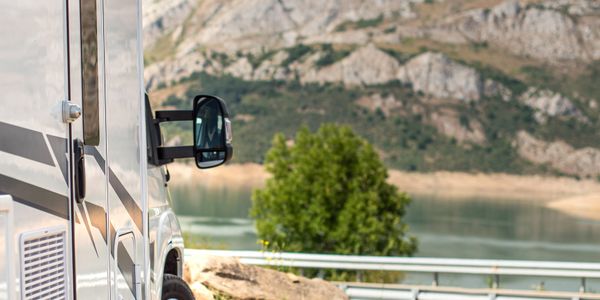 Side view of a white camper van parked near a lake with mountains in the background.