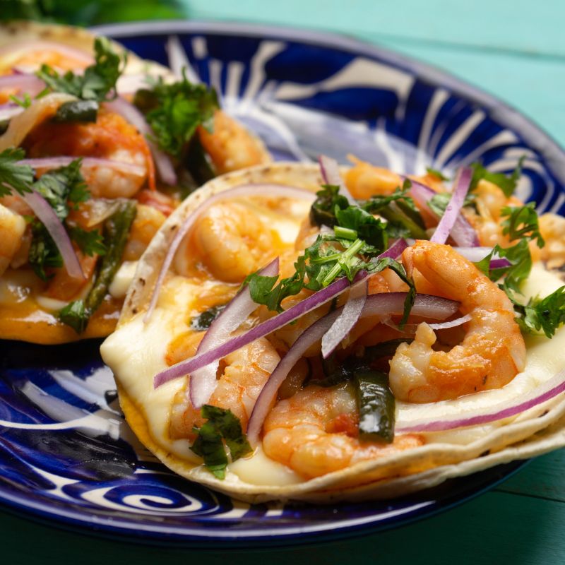 Traditional mexican food. Shrimp tacos with melted cheese and poblano pepper called gobernador on turquoise background.
