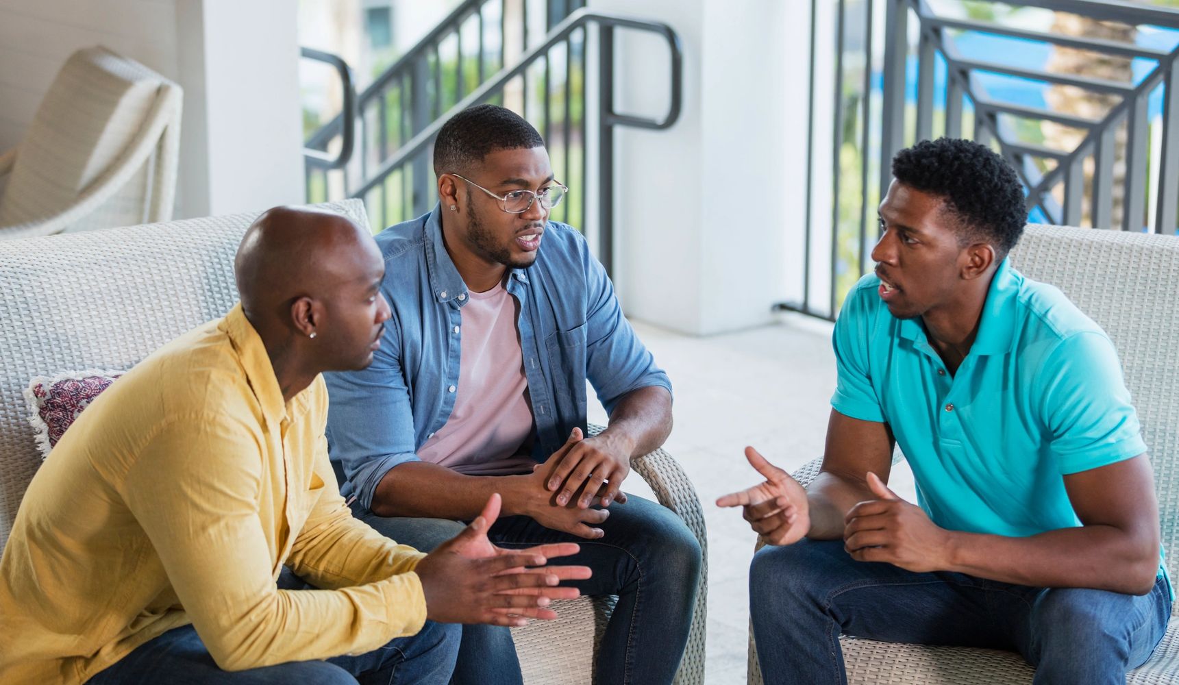 Three men engaged in a focused conversation on outdoor chairs.