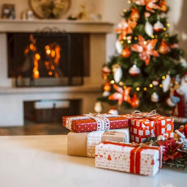 Christmas presents on a table with a decorated tree and fireplace in the background.