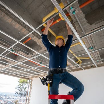 Worker wearing yellow helmet fixing ceiling pipes.