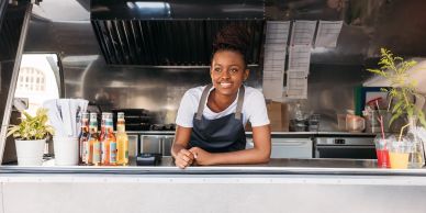 Smiling vendor in a food truck leaning on the counter.