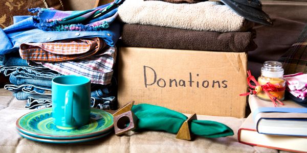 Box labeled Donations with clothes, plates, books, and a candle ready to give away.