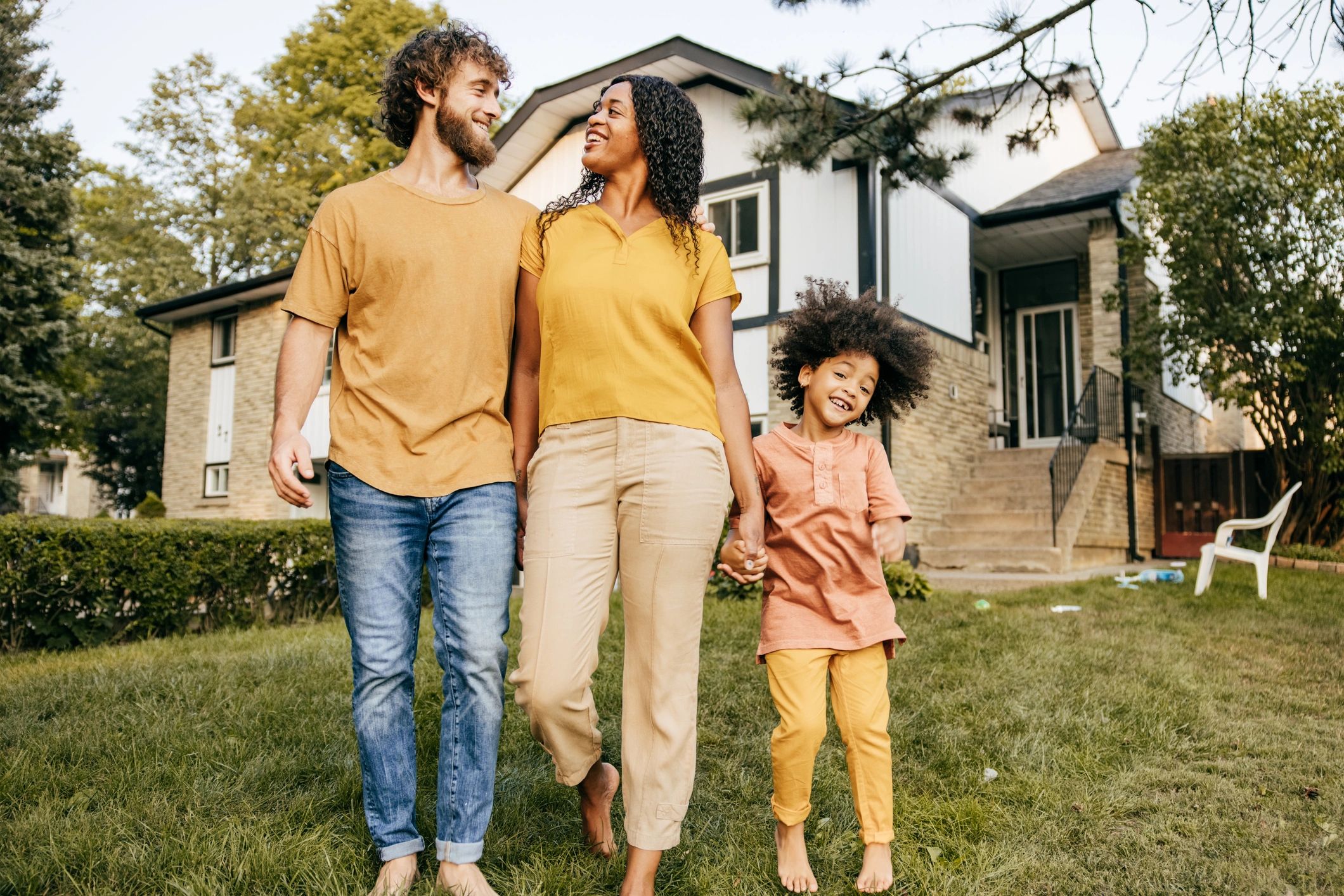 Happy family walking on grass in front of their house.