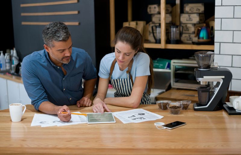 Latin American business owner doing to the books at a cafe with a waitress using a tablet computer - small business concepts. **DOCUMENTS AND DESIGN ON SCREEN WERE MADE FROM SCRATCH BY US**