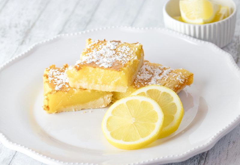 Yellow lemon bars homemade with slices of lemons on a white plate