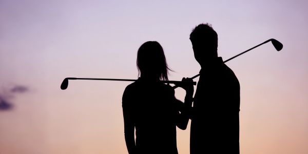 A golfer putting on a green during sunset.