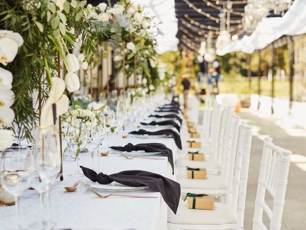 Elegant outdoor dining setup with white chairs, black napkins, and floral decor.