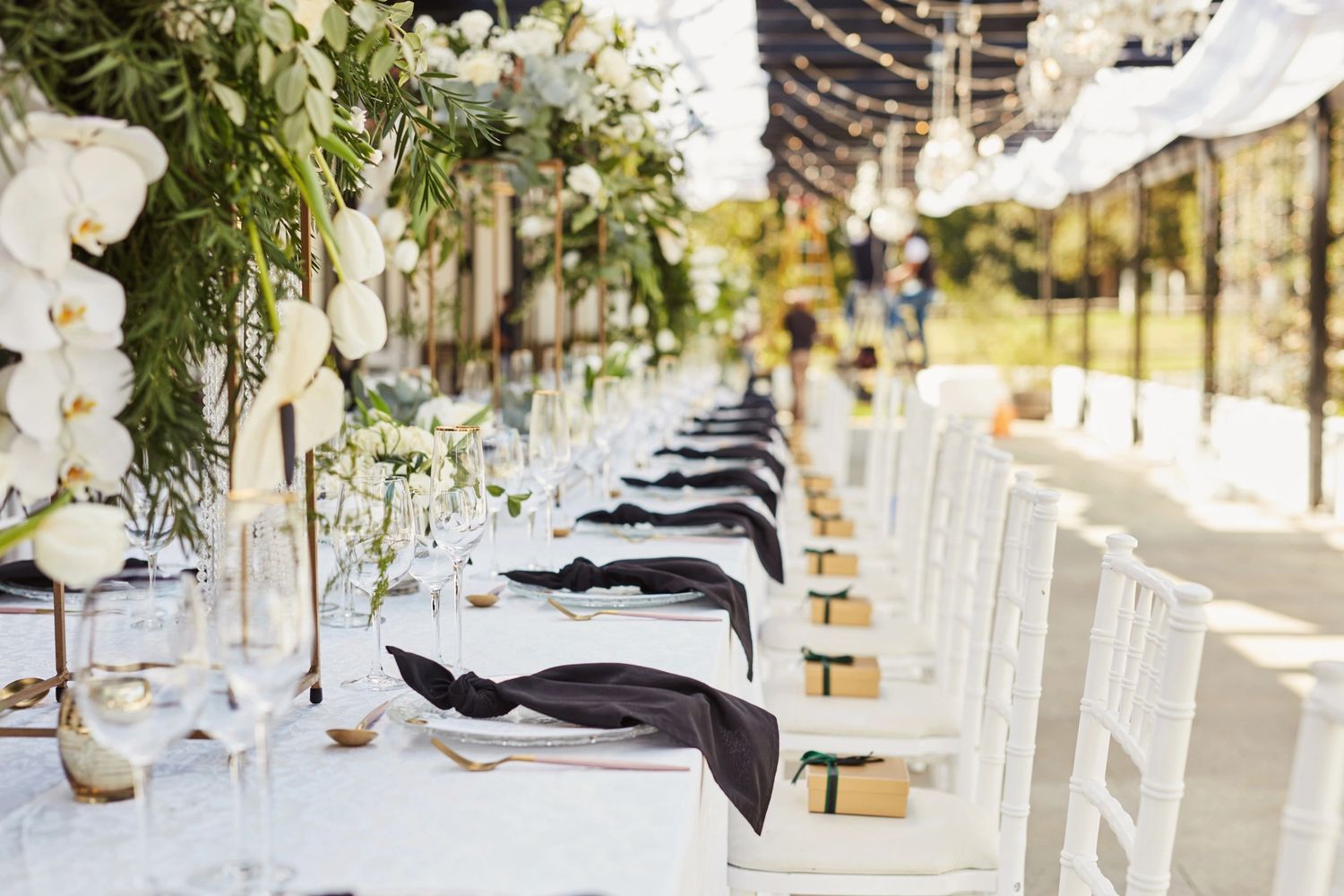 Elegant outdoor dining setup with white chairs, black napkins, and floral decor.