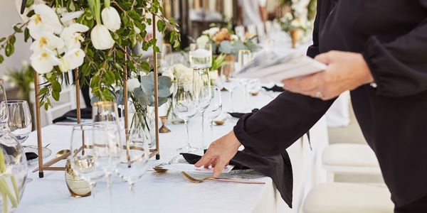 Person arranging elegant table settings with flowers and glassware.