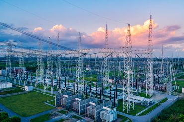 Electric power substation with towers under a vibrant sunset sky.