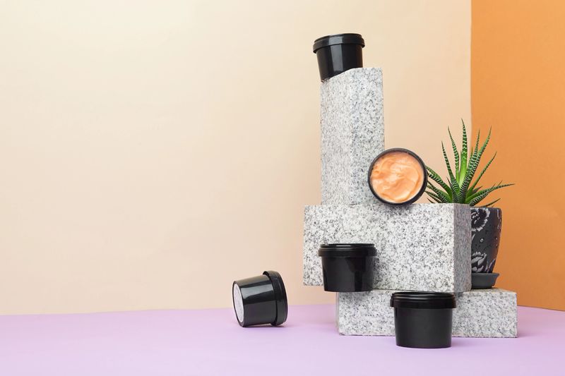 Natural products for body and face skin care. Variants of cream in black jars on a purple and beige background