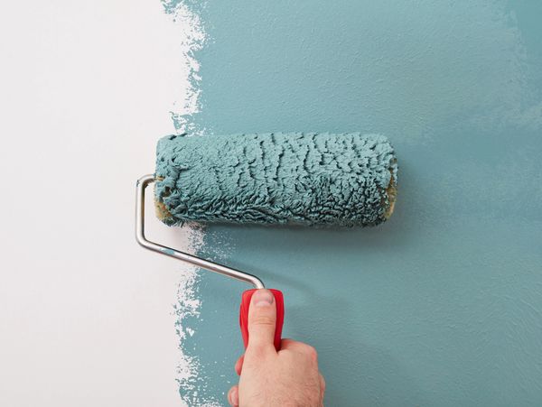 Hand using a paint roller to paint a wall teal over white.