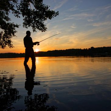 Silhouette of a person fishing at sunset by the lake.