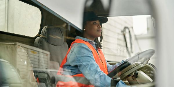 Woman in safety vest driving a vehicle.